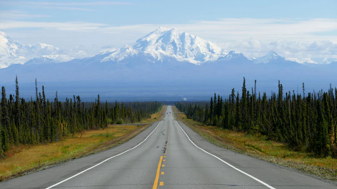 Empty Alaska highway leading toward a snow-capped mountain